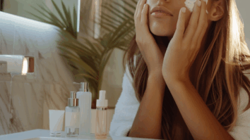 Mulher com as mãos no rosto e produtos de skincare expostos na pia do banheiro
